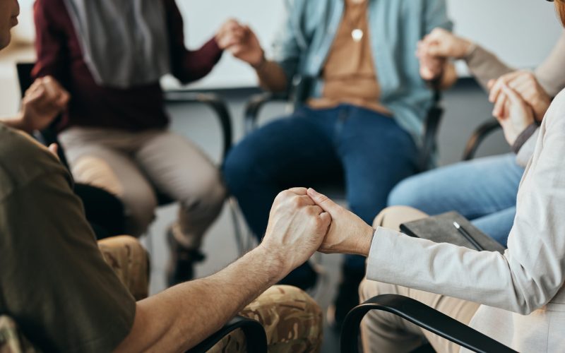 Close-up of people holding hands while sitting in a circle during group therapy at mental health center.