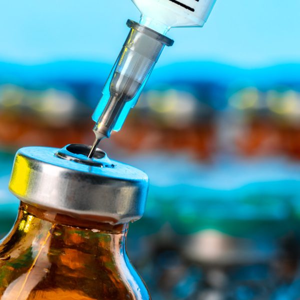 Vaccine bottle with a syringe taking the vaccine from it close up.